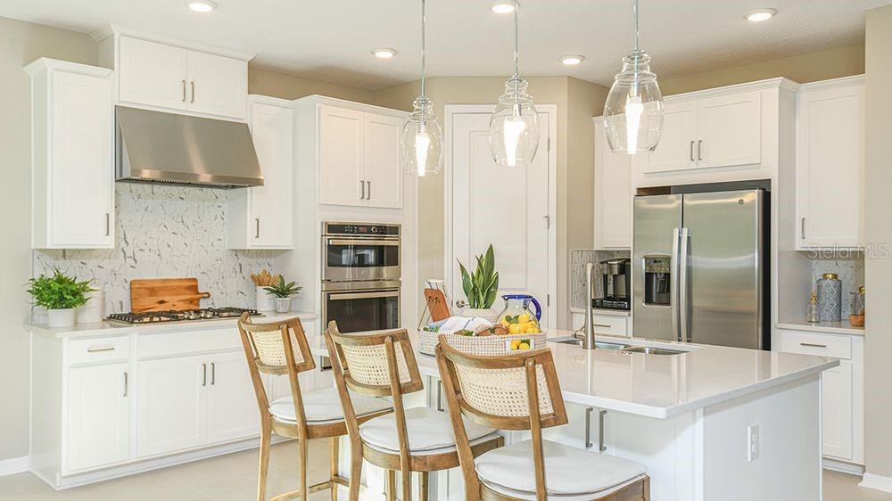 A modern kitchen features white cabinetry, stainless steel appliances, a marble backsplash, and a central island — 10 ARMENIA COURT, PALM COAST, FL