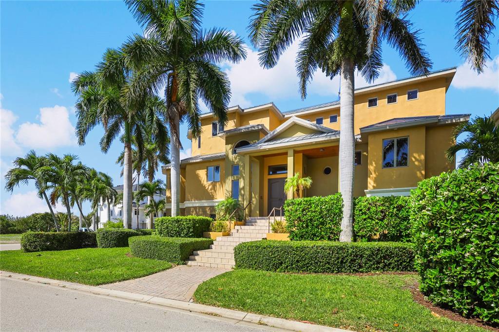 A two-story yellow house with palm trees, a brick walkway, and stairs leading to the entrance — 7158 HAWKS HARBOR CIRCLE, BRADENTON, FL
