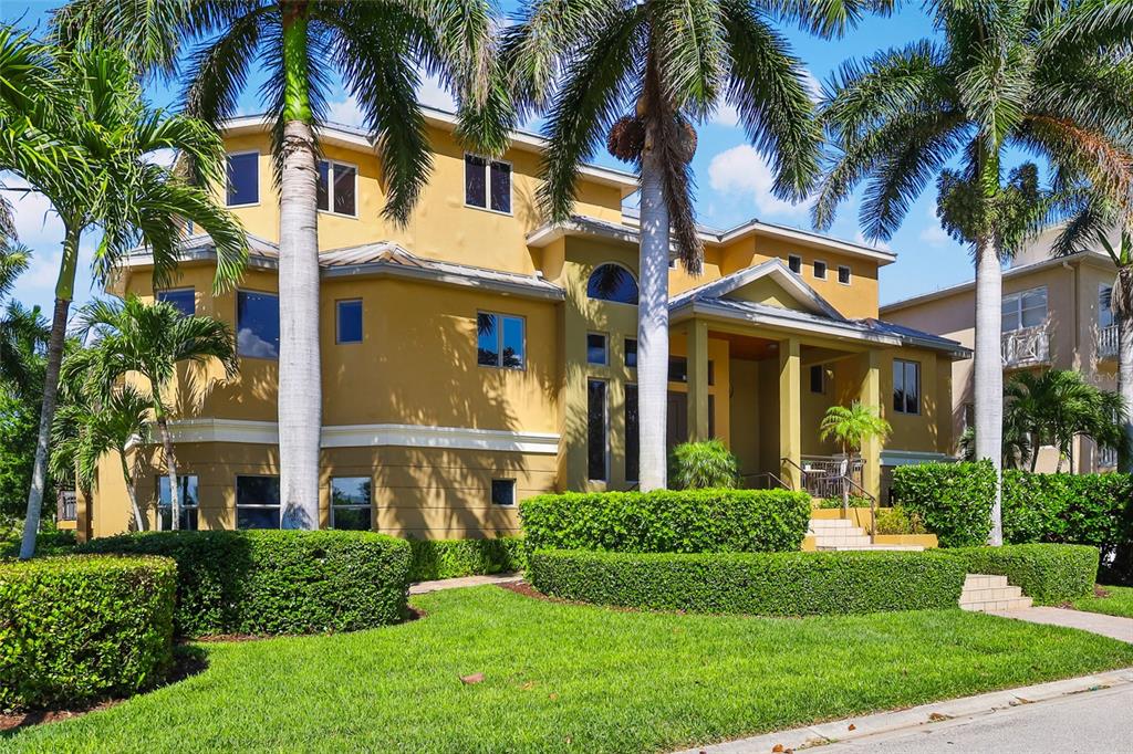 A yellow multi-story house with palm trees and manicured hedges in the front yard — 7158 HAWKS HARBOR CIRCLE, BRADENTON, FL