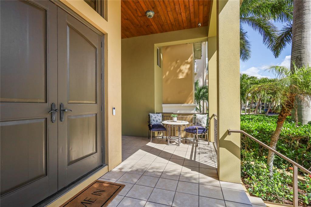 A covered patio features tiled flooring, a small bistro set, and double entry doors — 7158 HAWKS HARBOR CIRCLE, BRADENTON, FL