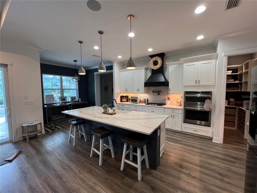 A modern kitchen features a large white quartz island, dark blue cabinetry, and stainless steel appliances — 6233 RIVO LAKES BOULEVARD, SARASOTA, FL