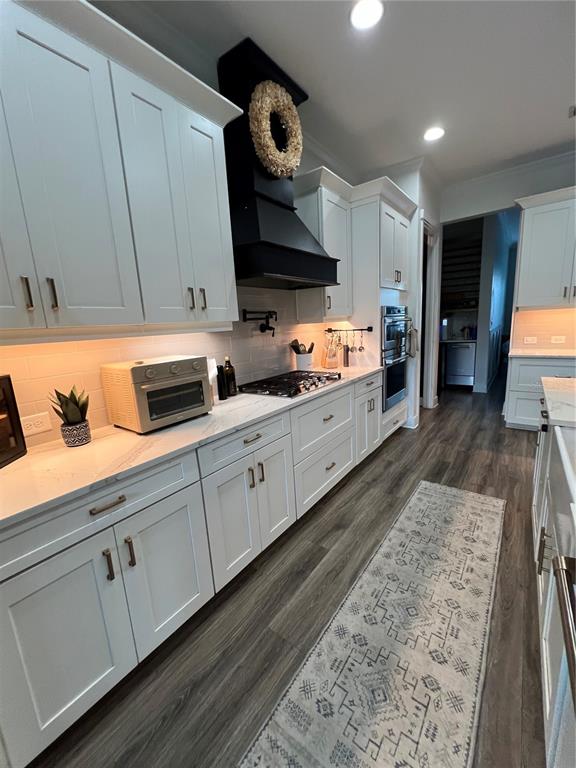 A kitchen features white cabinets, a black range hood, stainless steel appliances, and wood-look flooring — 6233 RIVO LAKES BOULEVARD, SARASOTA, FL