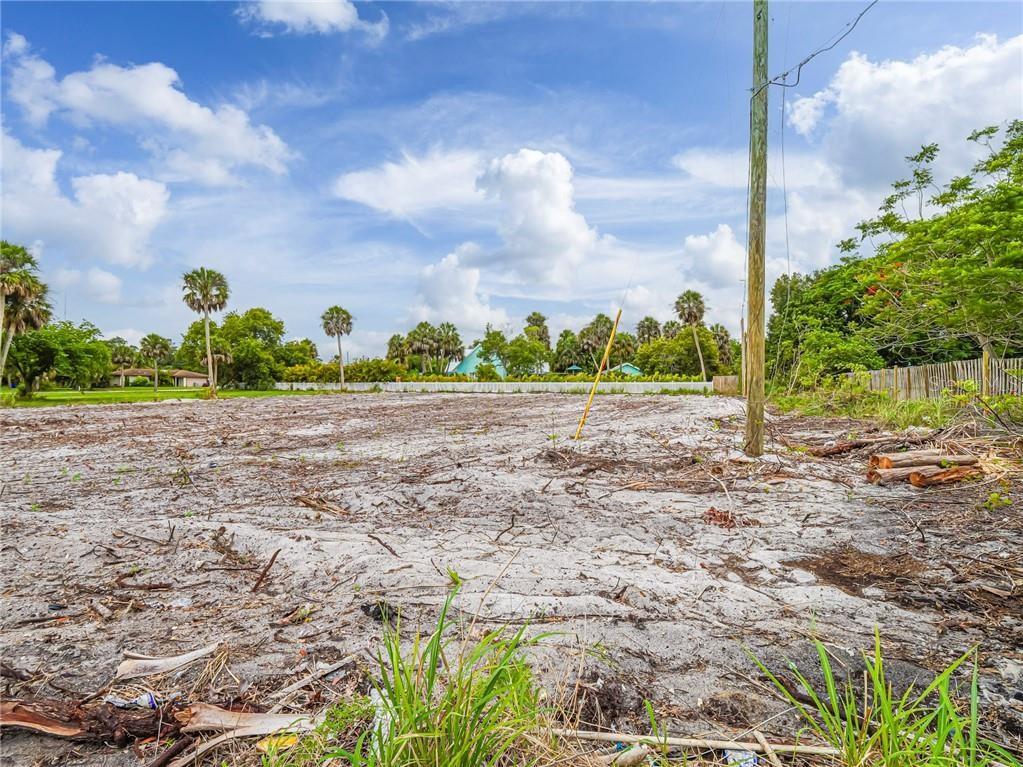 A cleared, sandy vacant lot features a utility pole and scattered vegetation under a blue sky — 445 OLD DIXIE HIGHWAY, VERO BEACH, FL