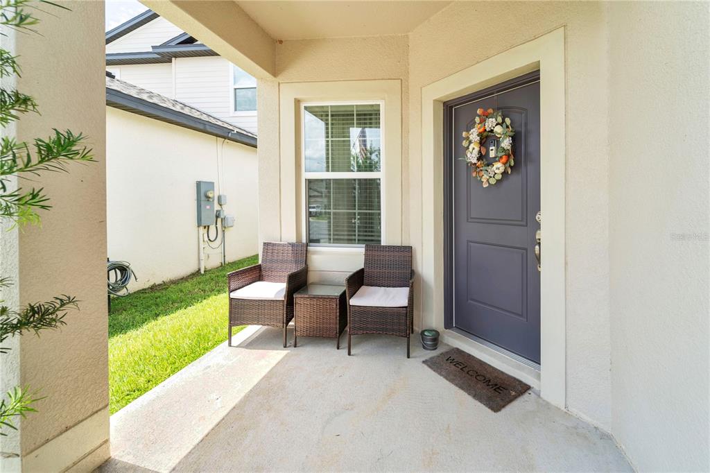 A covered front porch features two wicker chairs, a small table, and a gray door — 5261 FEZ COURT, BROOKSVILLE, FL