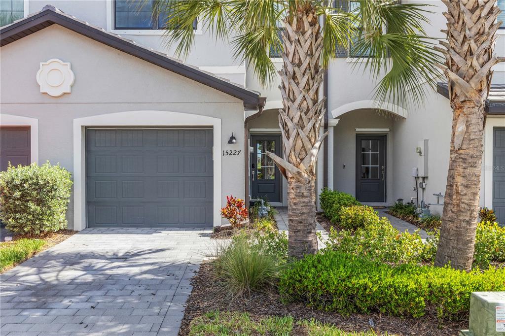 A two-story townhouse exterior features a gray garage, two front doors, and palm trees — 15227 SUNNY DAY DRIVE, BRADENTON, FL