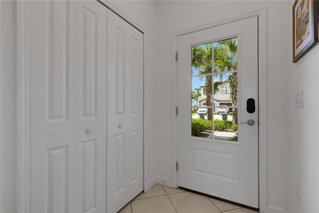An entryway features white walls, tiled flooring, a double-door closet, and a glass-paneled front door — 15227 SUNNY DAY DRIVE, BRADENTON, FL