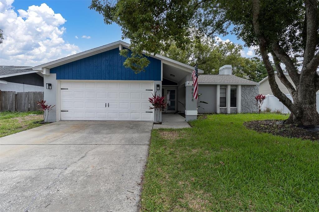 A house exterior features a blue and gray facade, a front porch, and an American flag — 8038 BUTTONBALL LANE, PORT RICHEY, FL