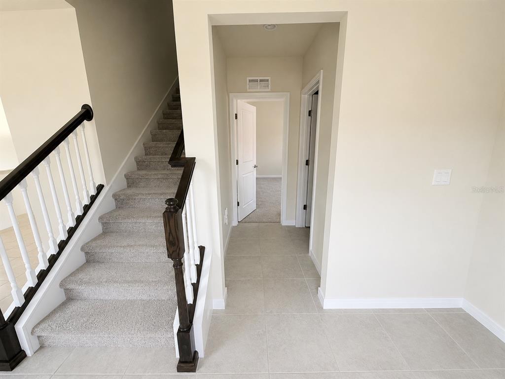 A carpeted staircase with a dark wood railing leads upstairs next to a tiled hallway — 4083 FEATHER TREE DRIVE, APOPKA, FL