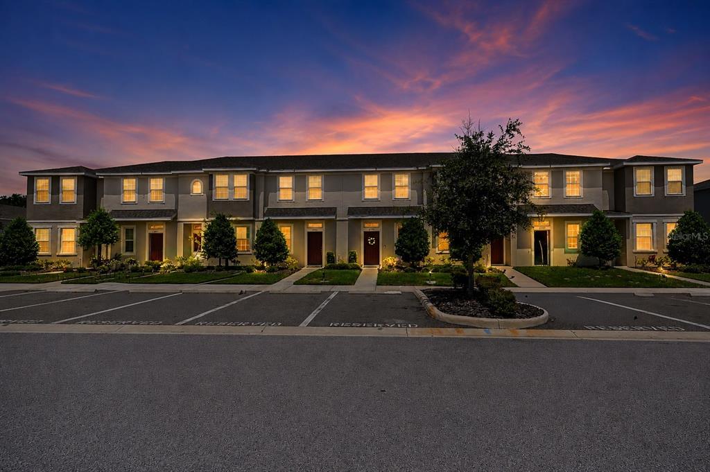 A multi-unit townhouse building exterior at dusk with a parking lot in the foreground — 6130 FAIRMONT LANE, PALMETTO, FL