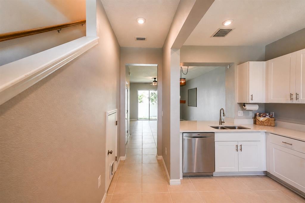 A kitchen with white cabinets and stainless steel appliances leads to a hallway with stairs — 6130 FAIRMONT LANE, PALMETTO, FL