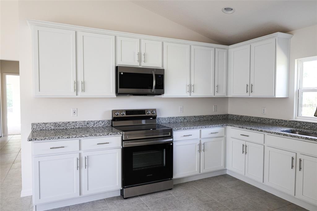 A kitchen with white cabinets, stainless steel appliances, and tile flooring under a vaulted ceiling — 79 W CENTRAL AVENUE, WEBSTER, FL