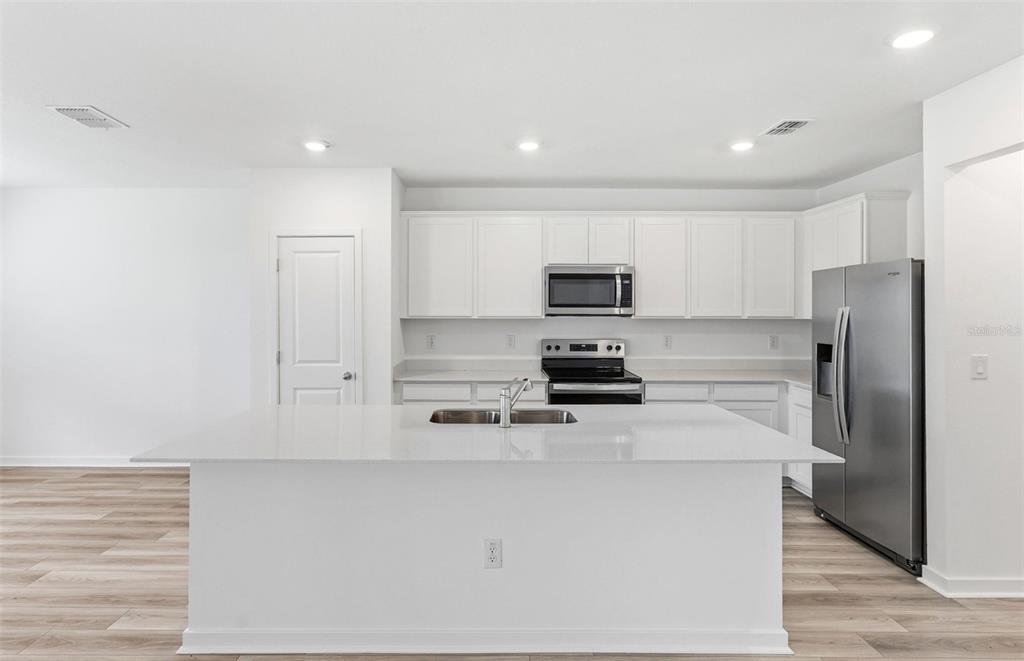 A modern kitchen features a large white island, stainless steel appliances, and white cabinetry — 10422 HIDDEN BANKS GLEN, PARRISH, FL