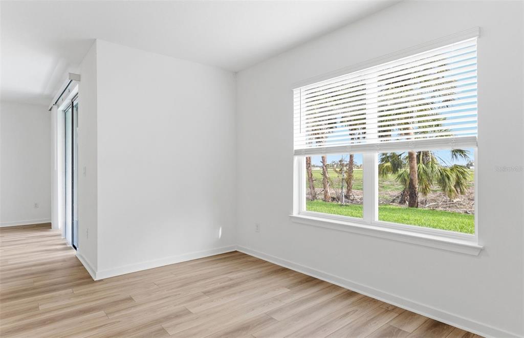 An empty room with light wood-look flooring, white walls, and a window overlooking palm trees — 10422 HIDDEN BANKS GLEN, PARRISH, FL
