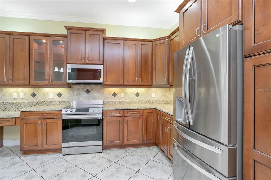 A kitchen features wood cabinets, granite countertops, stainless steel appliances, and tiled flooring — 16022 GOLDEN LAKES DRIVE, WIMAUMA, FL