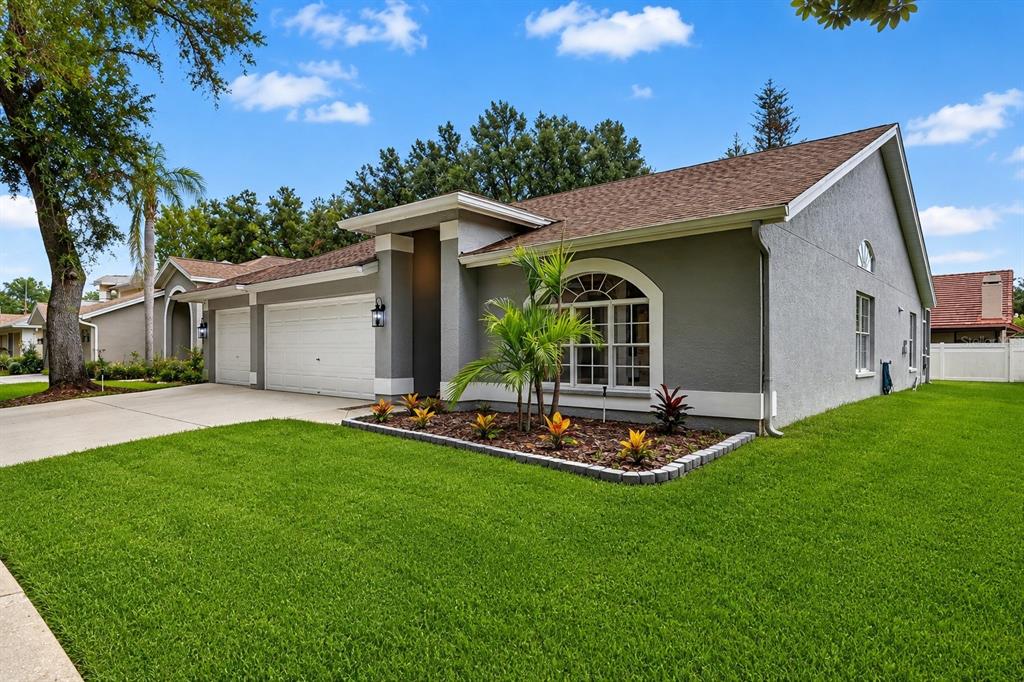 A gray single-story house with a two-car garage, arched window, and landscaped front yard — 17721 HAMPSHIRE OAK DRIVE, TAMPA, FL