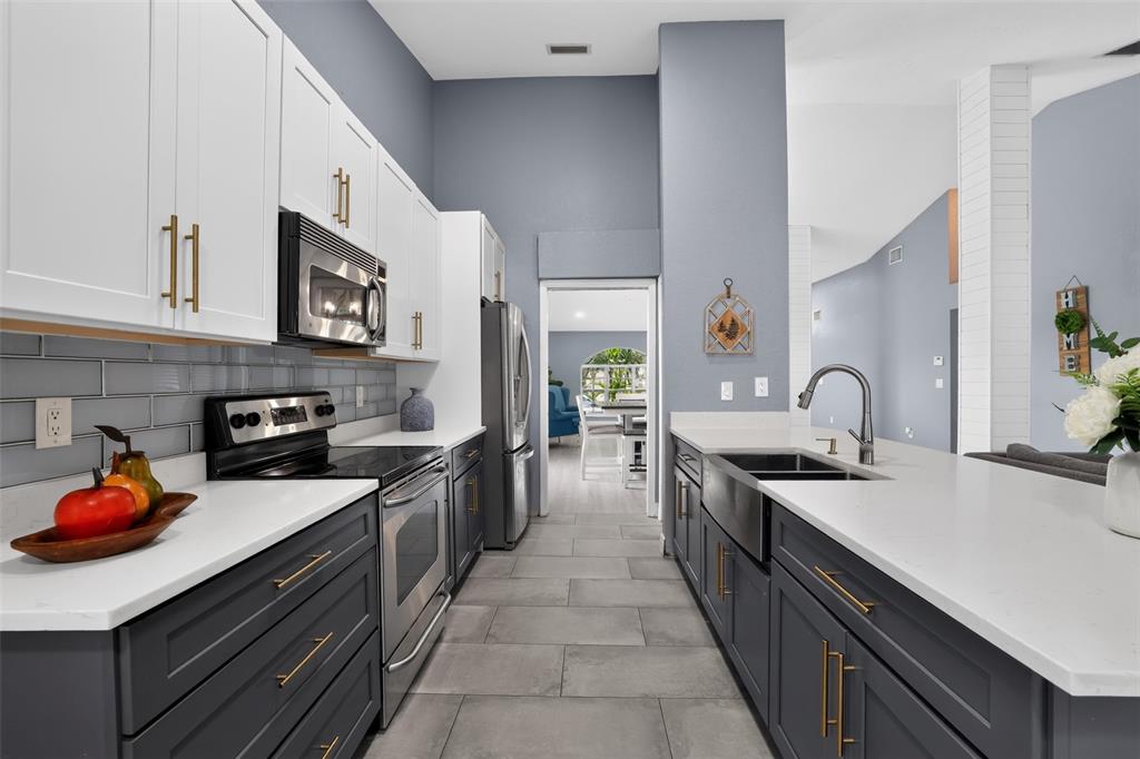 A modern kitchen features dark gray lower cabinets, white upper cabinets, and a farmhouse sink — 17721 HAMPSHIRE OAK DRIVE, TAMPA, FL