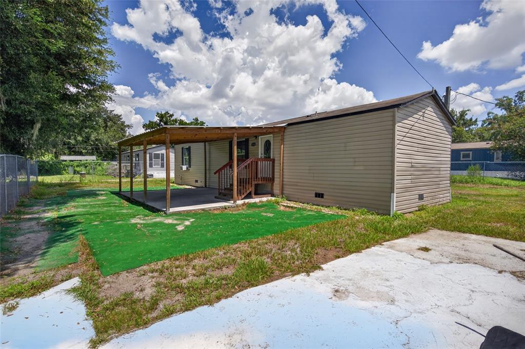 A tan mobile home with a covered porch and a concrete patio in the yard — 1414 EVA AVENUE, LAKELAND, FL