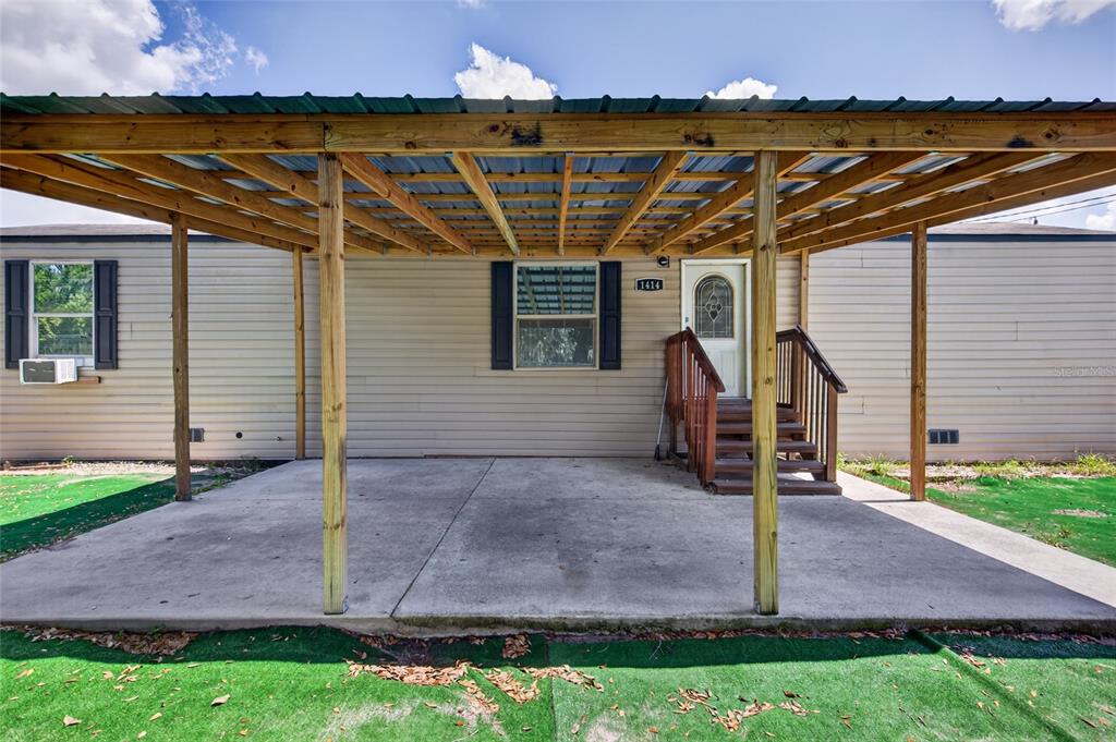 A concrete patio covered by a wooden pergola sits in front of a tan mobile home — 1414 EVA AVENUE, LAKELAND, FL