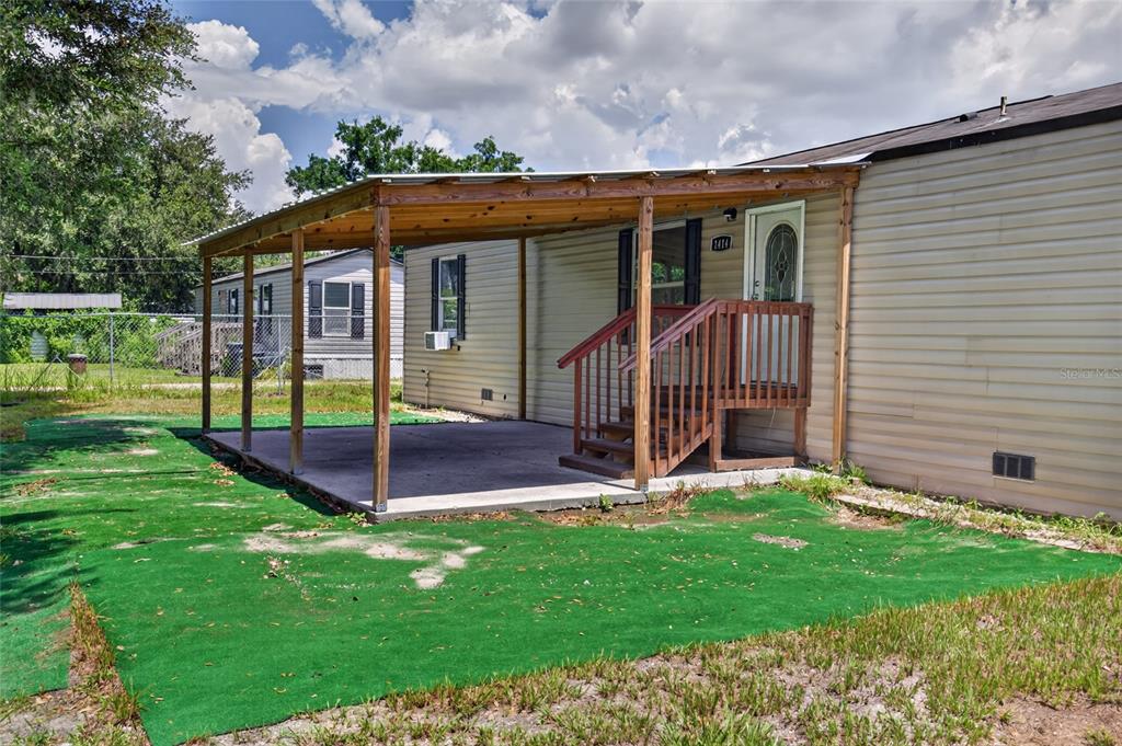 A mobile home exterior features a covered concrete patio and wooden stairs leading to a door — 1414 EVA AVENUE, LAKELAND, FL