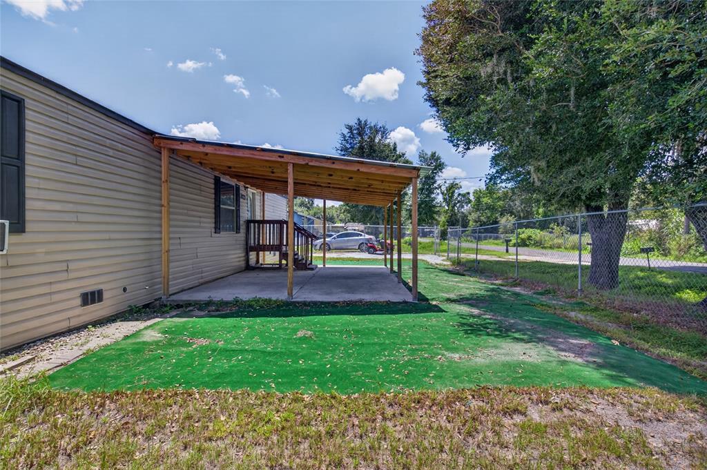 A side view of a mobile home featuring a covered concrete patio and artificial turf — 1414 EVA AVENUE, LAKELAND, FL