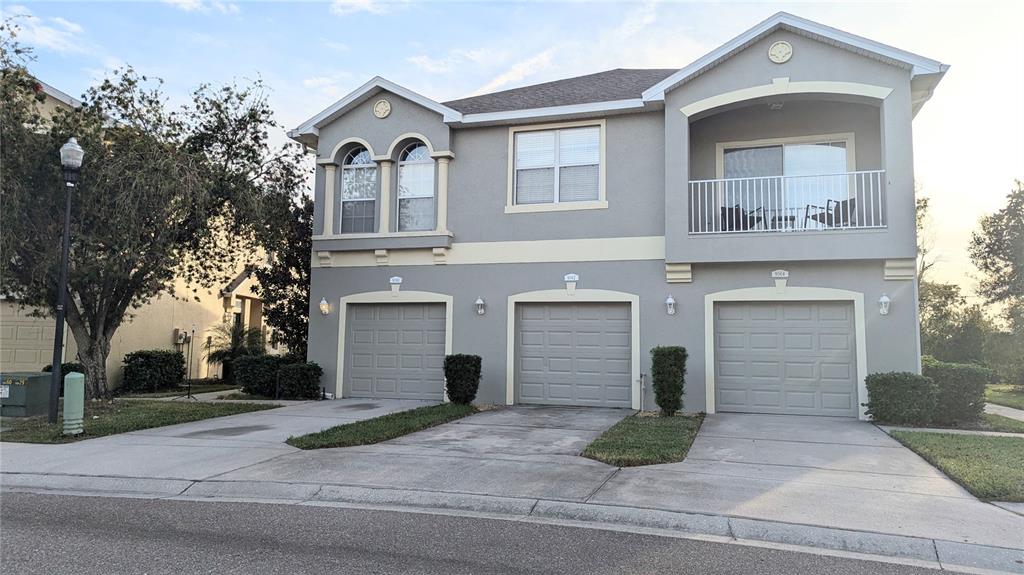 A three-unit residential building features gray stucco siding, three garage doors, and an upper balcony — 9060 MOONLIT MEADOWS LOOP, RIVERVIEW, FL