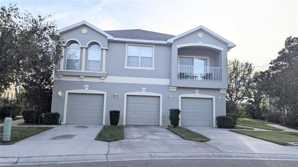 A three-unit townhouse building with gray stucco siding, three garage doors, and a second-story balcony — 9060 MOONLIT MEADOWS LOOP, RIVERVIEW, FL
