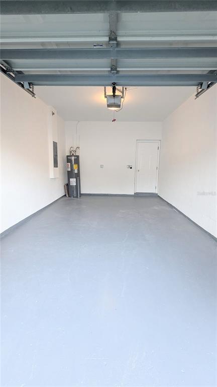 An empty garage with a gray concrete floor, a water heater, and a white door — 9060 MOONLIT MEADOWS LOOP, RIVERVIEW, FL