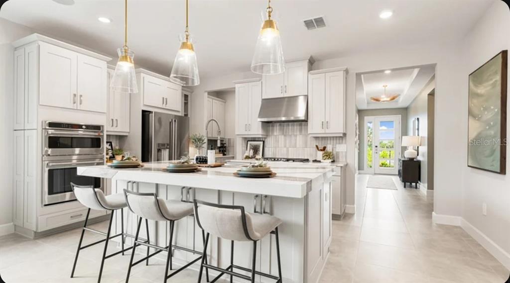 A modern kitchen features white cabinetry, a large island with bar seating, and stainless appliances — 725 SKY SHADE DRIVE, APOLLO BEACH, FL