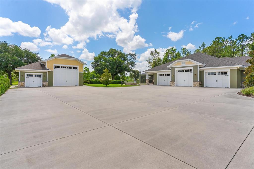 A large concrete driveway sits between two detached garage buildings with green siding — 10615 NE 104TH CIRCLE, OXFORD, FL