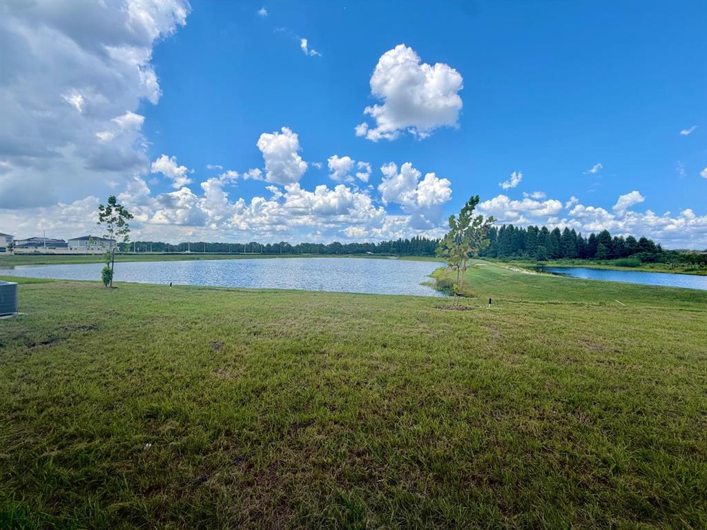 A grassy backyard overlooks a large pond under a bright blue sky with scattered clouds — 6213 BOTTICELLA BOULEVARD, WINTER HAVEN, FL