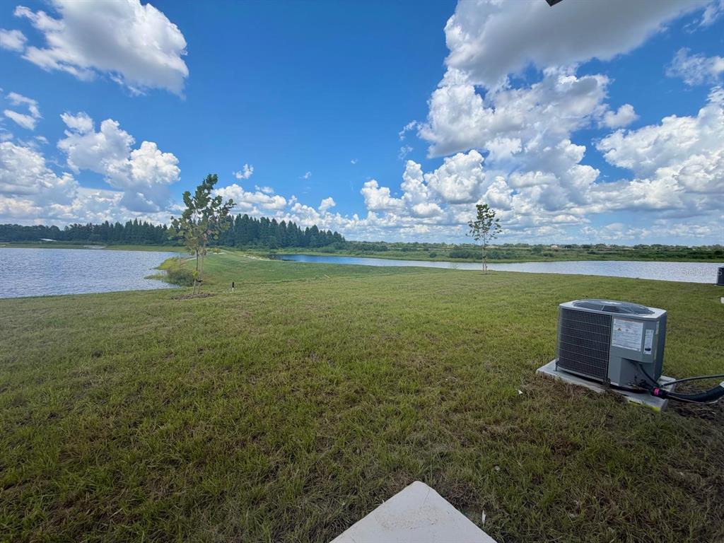 A grassy backyard overlooks a lake under a bright blue sky with scattered clouds — 6213 BOTTICELLA BOULEVARD, WINTER HAVEN, FL