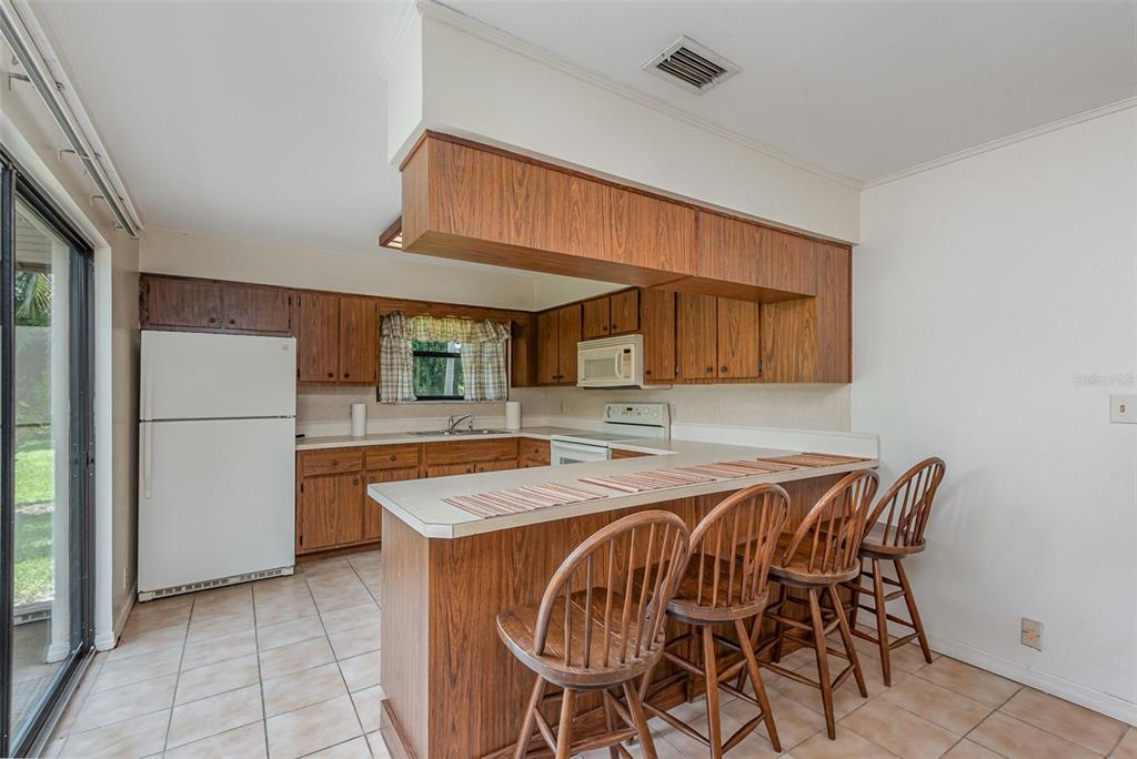 A kitchen with wood cabinets, a breakfast bar, and four wooden chairs on tile flooring — 4300 JUSTA ROAD, MIMS, FL