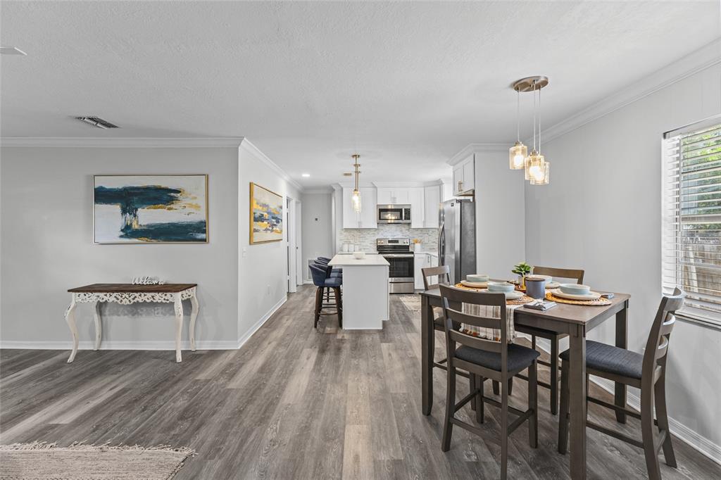 A dining area and kitchen feature white cabinets, stainless steel appliances, and wood-look flooring — 1008 37TH STREET W, BRADENTON, FL