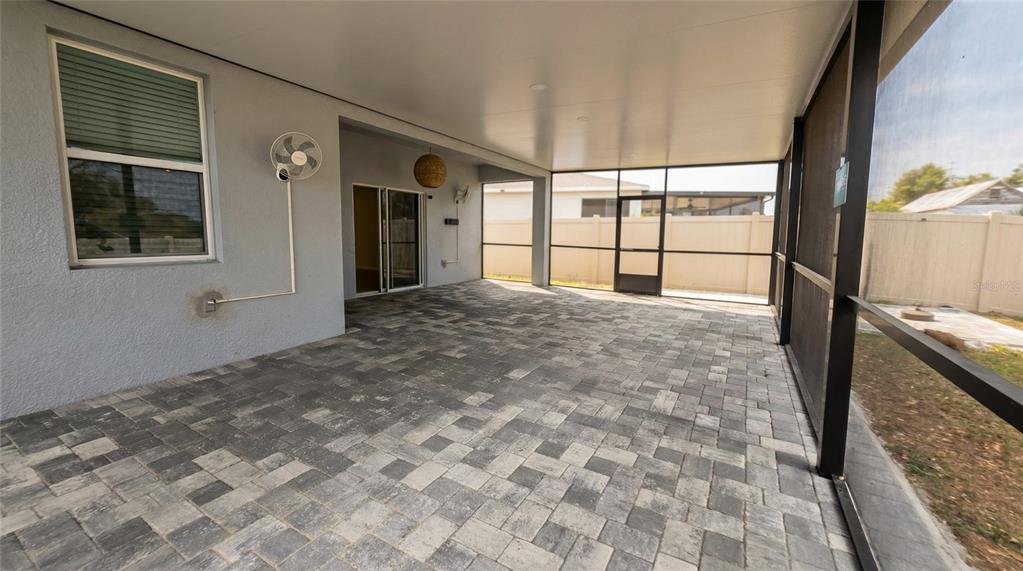 A covered patio features gray paver flooring, a screen enclosure, and a wall-mounted fan — 693 CROWN ROSE DRIVE, EAGLE LAKE, FL