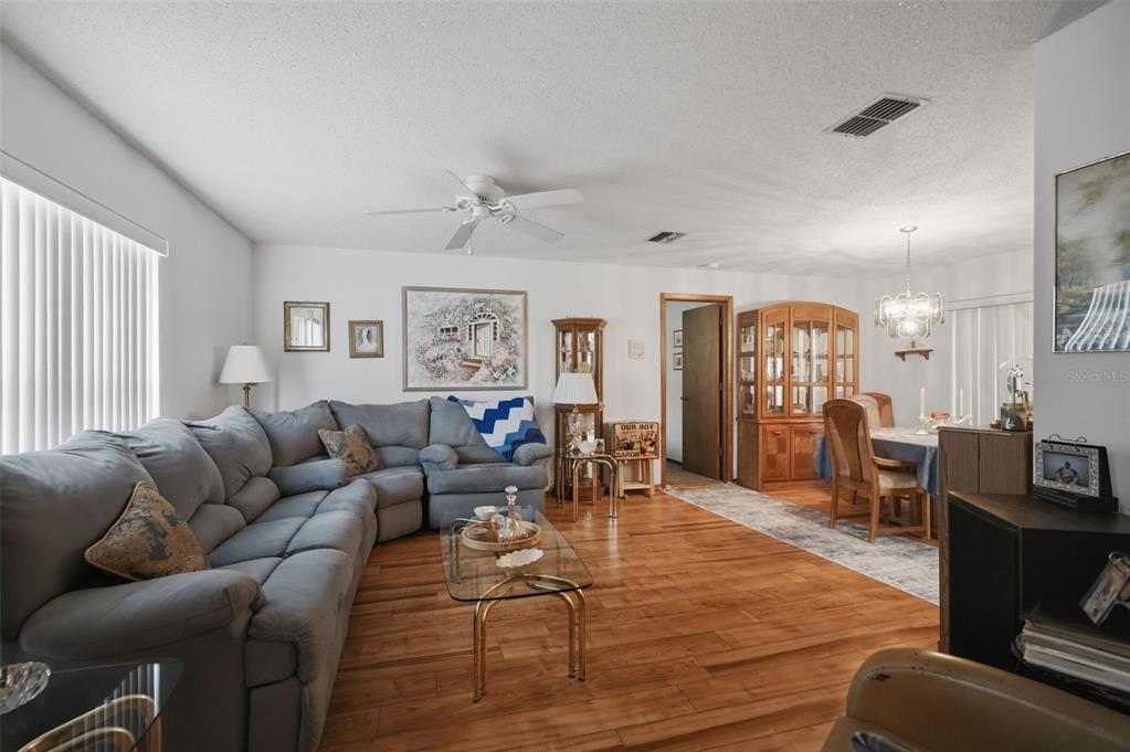 A living room with wood flooring, a grey sectional sofa, and an adjacent dining area — 11333 SILVERWOOD COURT, SPRING HILL, FL