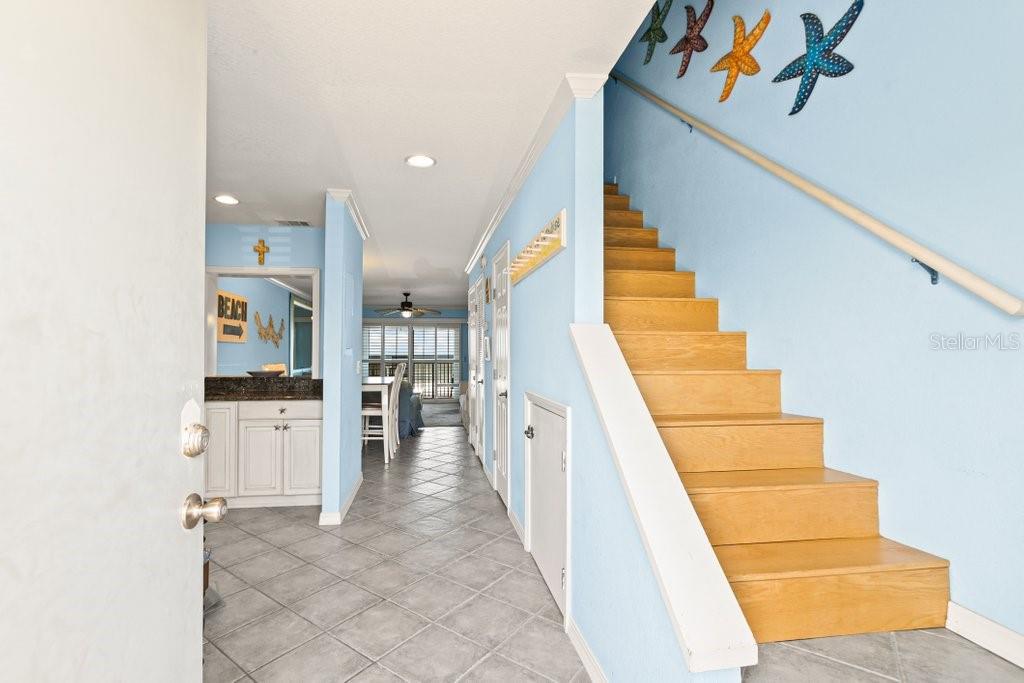 An entryway with light blue walls, tile flooring, and a wooden staircase leading upstairs — 8550 A1A #208 S UNIT 2128, ST AUGUSTINE, FL
