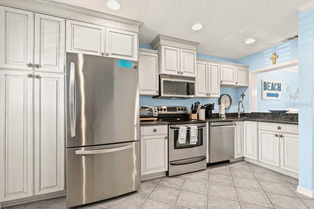 A kitchen featuring white cabinets, stainless steel appliances, dark countertops, and light blue walls — 8550 A1A #208 S UNIT 2128, ST AUGUSTINE, FL