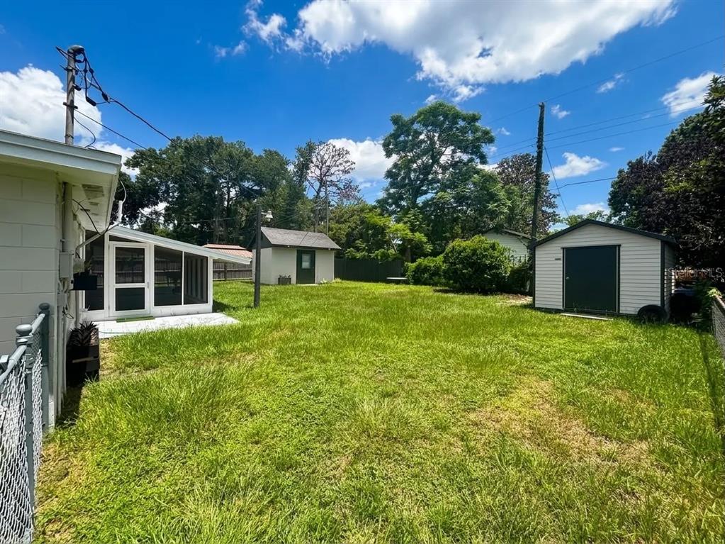 A grassy backyard features a white house with a screened porch and two detached sheds — 1532 E VOTAW ROAD, APOPKA, FL