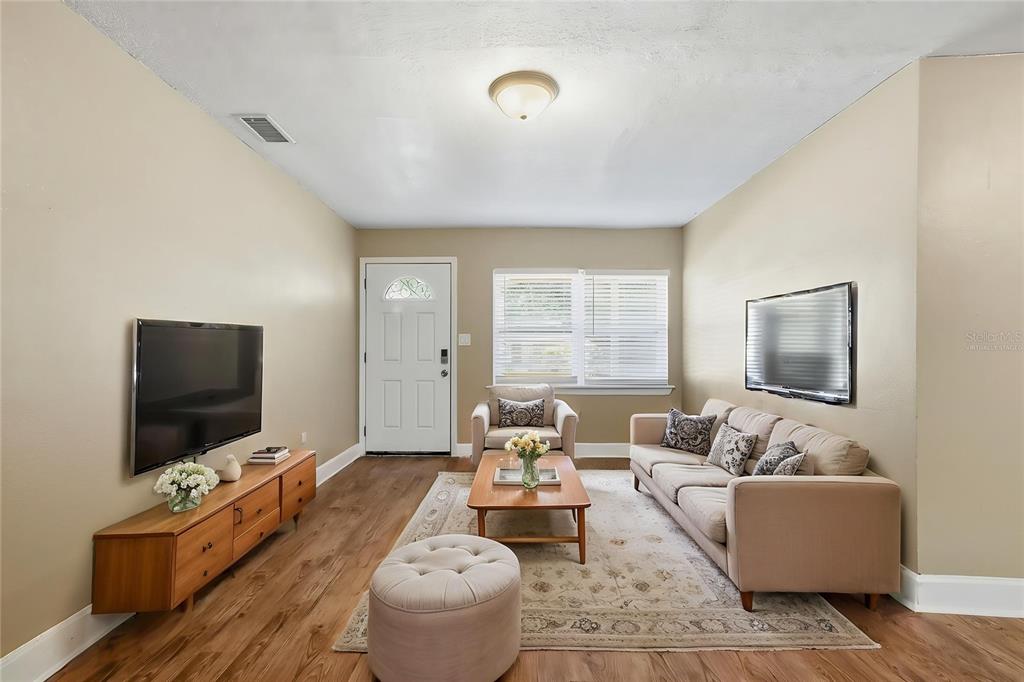 A living room features light wood flooring, a beige sofa, a television, and a front door — 3521 ARCH STREET, ORLANDO, FL