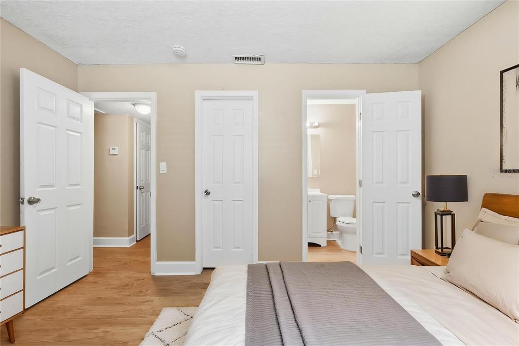 A bedroom features light wood flooring, beige walls, three white doors, and an en suite bathroom — 3521 ARCH STREET, ORLANDO, FL