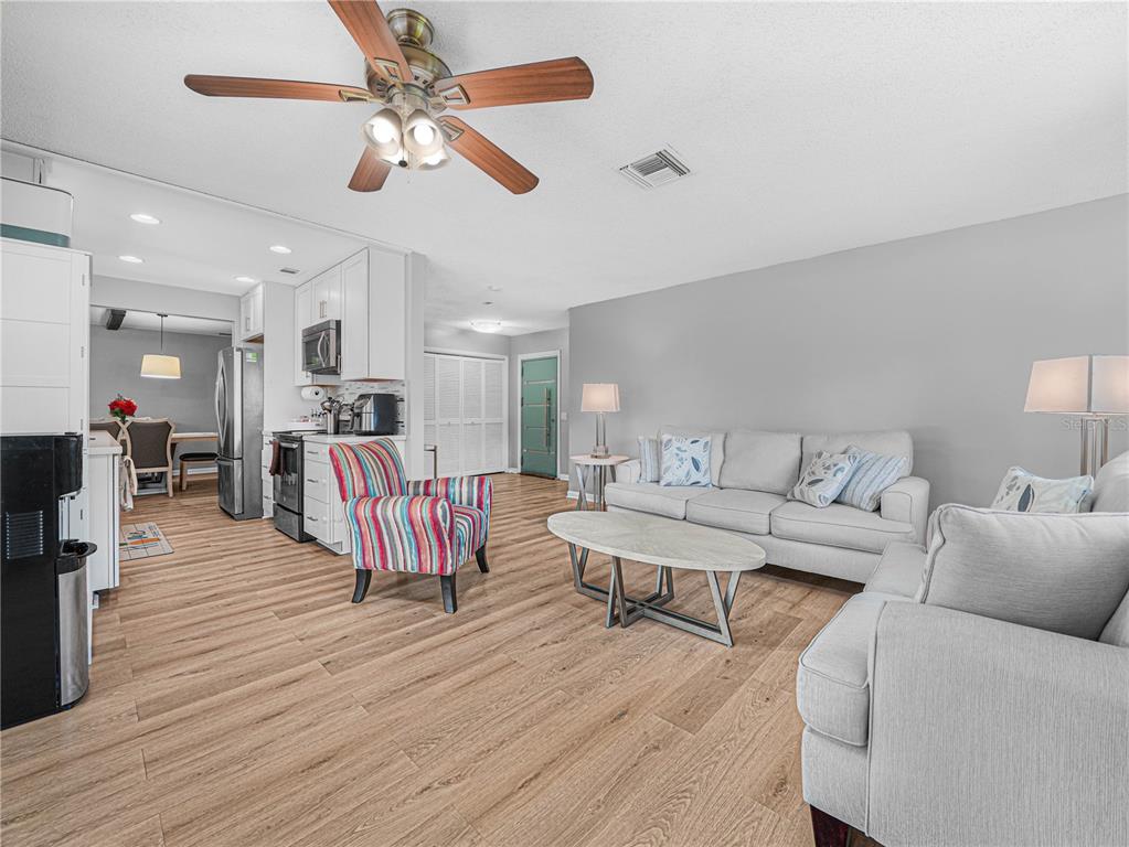 A living room with wood-look flooring, a light gray sofa, and a colorful patterned armchair — 437 BROWARD TERRACE, WINTER HAVEN, FL