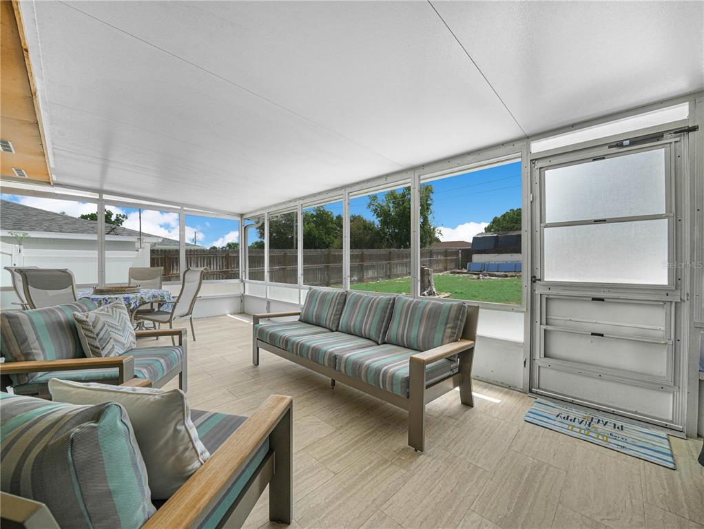 A screened-in porch features tiled flooring, outdoor furniture, and a view of a fenced backyard — 437 BROWARD TERRACE, WINTER HAVEN, FL