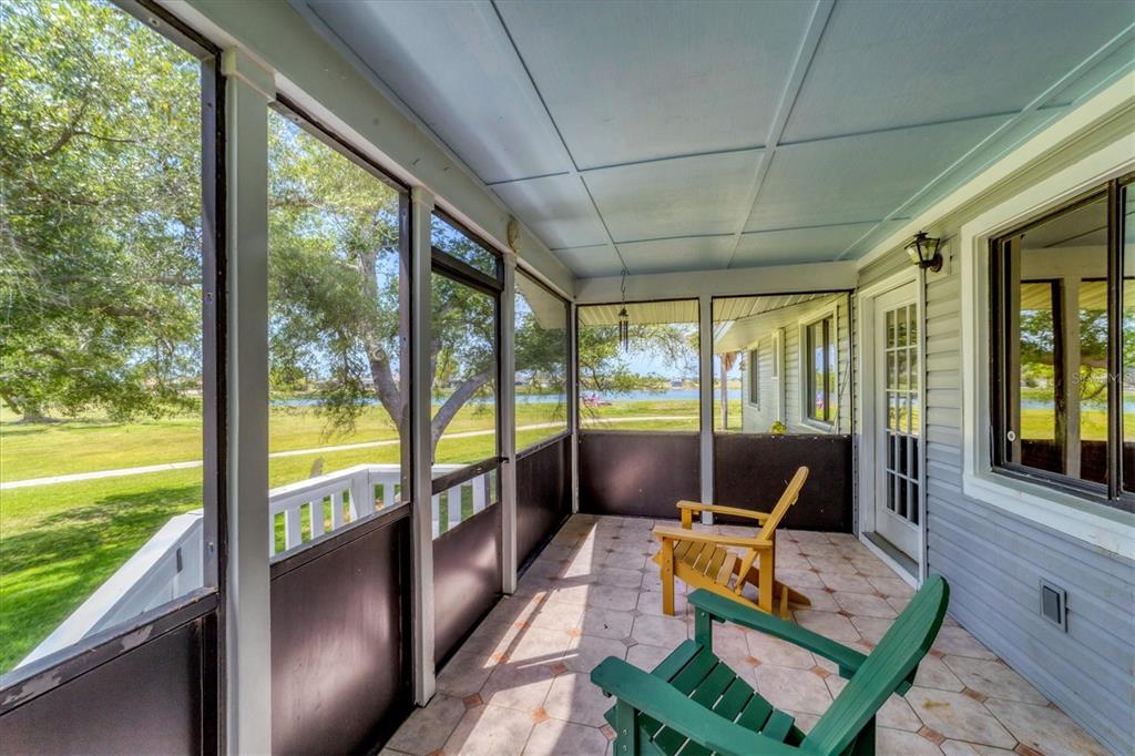 A screened-in porch with tiled flooring, two wooden chairs, and a view of a lake — 18 PEBBLE BEACH ROAD, ROTONDA WEST, FL