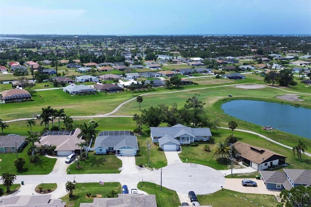 An aerial view shows suburban houses surrounding a golf course with a pond — 18 PEBBLE BEACH ROAD, ROTONDA WEST, FL