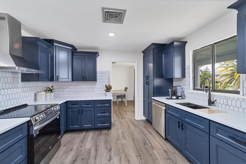 A kitchen features dark blue cabinets, white countertops, a white tile backsplash, and wood flooring — 18 PEBBLE BEACH ROAD, ROTONDA WEST, FL