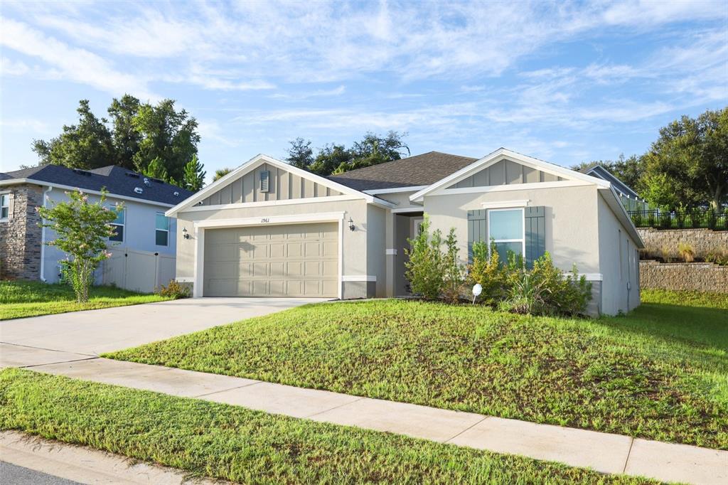 A single-story suburban house with a tan stucco exterior, two-car garage, and a front lawn — 1961 BURGUNDY DRIVE, MINNEOLA, FL