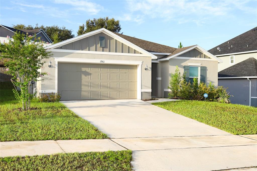 A single-story house with a beige stucco exterior, a two-car garage, and a concrete driveway — 1961 BURGUNDY DRIVE, MINNEOLA, FL