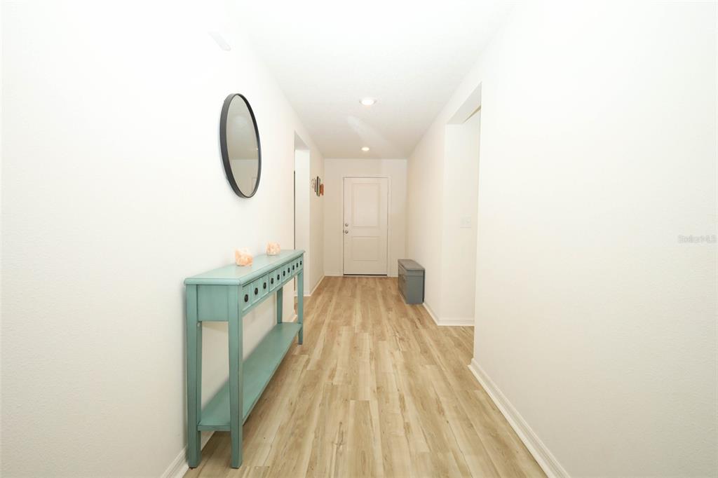 A hallway features light wood-look flooring, white walls, a teal console table, and a mirror — 1961 BURGUNDY DRIVE, MINNEOLA, FL