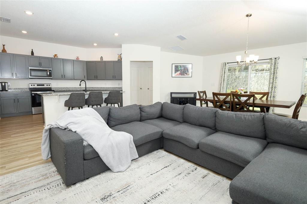 An open-concept living room with a gray sectional sofa, kitchen, and dining area — 1961 BURGUNDY DRIVE, MINNEOLA, FL