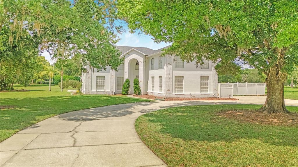 A two-story white brick house with a curved driveway sits on a grassy lot — 2152 BLUE IRIS PLACE, LONGWOOD, FL